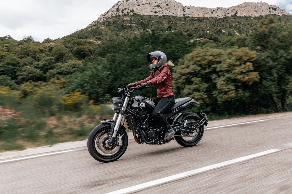 une motarde roulant sur la route en road-trip, elle porte tout son équipement de protection : casque, gants, veste, jean, bottes.